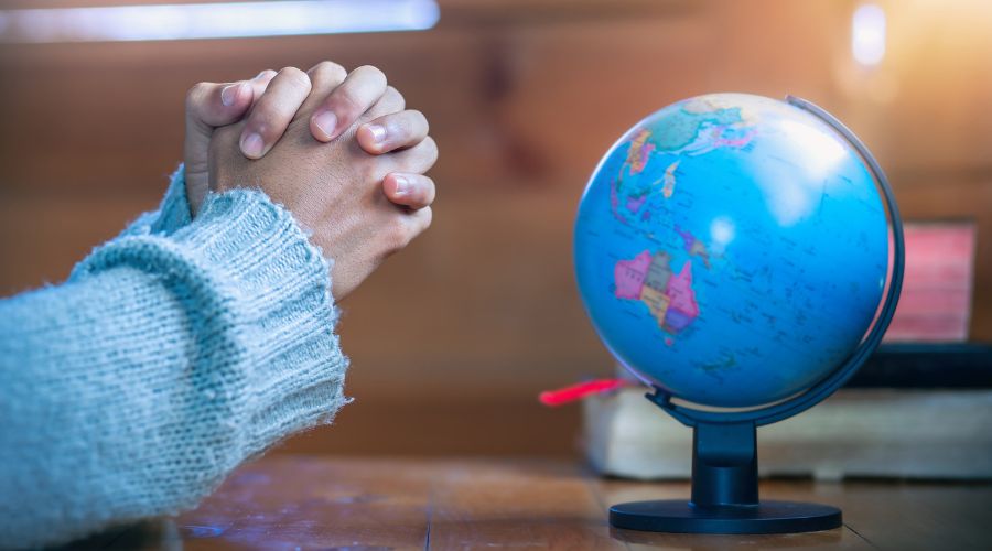 praying hands next to small globe