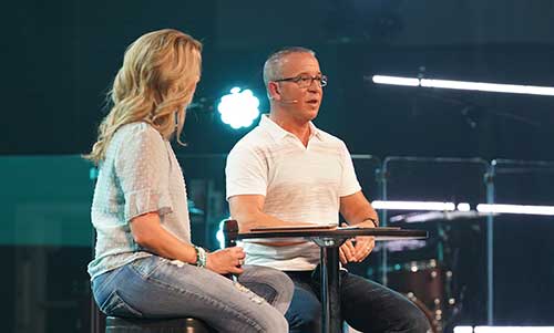 Pastor speaking on stage with wife